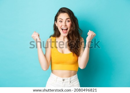 Summer holidays and emotions concept. Excited young woman winning and screaming from joy, achieve goal, celebrating victory, making fist pumps, standing over blue background ストックフォト © 