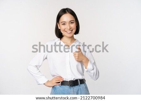 Photo of Image of confident asian woman showing thumb up in approval, recommending, like smth good, standing over white background