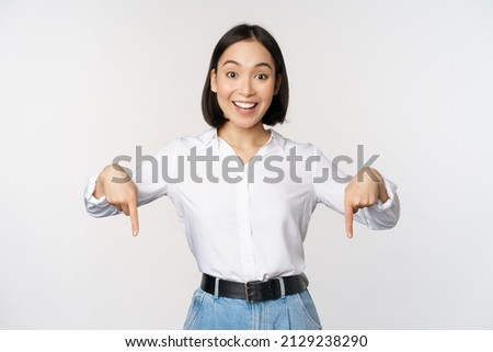 Portrait of young asian woman pointing fingers down and smiling, showing banner, click on link below gesture, inviting people to follow, standing over white background Stockfoto © 