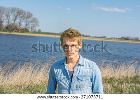 Young handsome man standing at water. Wearing blue blouse with sloppy hair
