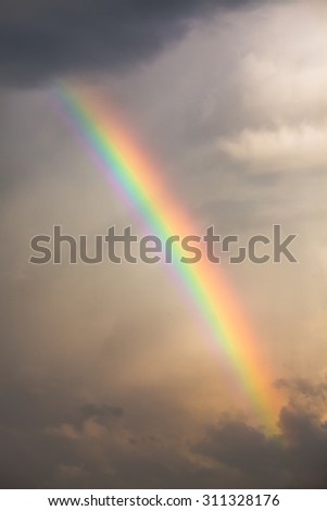 Bright rainbow between clouds in a grey, stormy sky