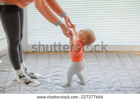 mother holding baby\'s hands to help him/her to walk over white background, windows