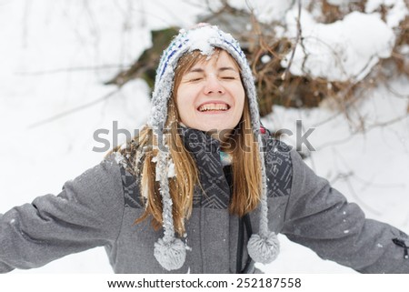 happy young girl with closed eyes catching falling snow with stretched arms outdoors