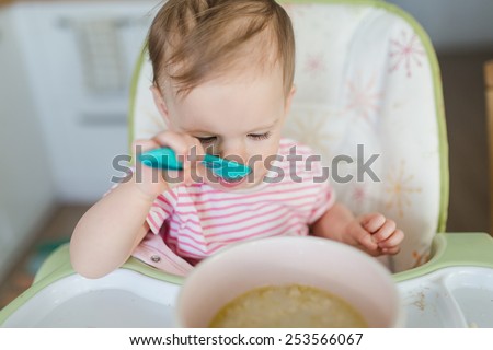 Baby girl having her meal and using a spoon to eat.  Baby eating porridge for breakfast.