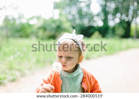 cute baby girl blowing a white dandelion in her hands