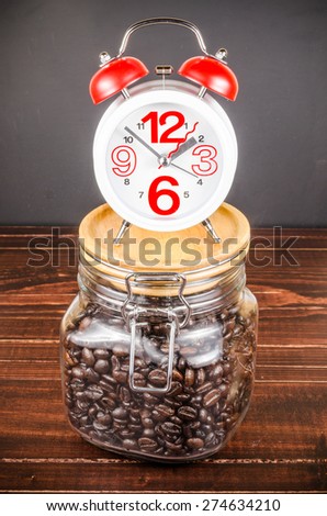 Coffee time,alarm clock with white coffee cup and coffee bean in glass bottle on wooden background