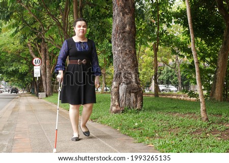 Asian blind person woman walking on sidewalk with a long white cane a mobility tool used to detect objects in the path, also helpful for onlookers in identifying the user as blind or vision disability Stock fotó © 