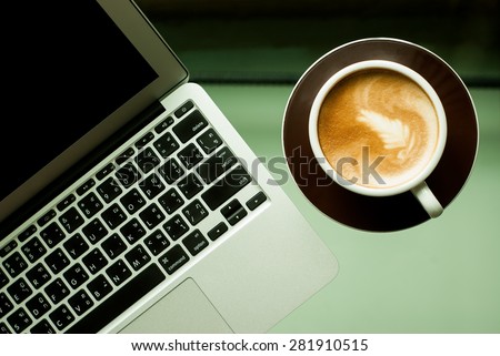 Perfect cup of hot coffee latte and laptop on glass desk