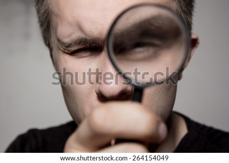 A man with a magnifying glass looking at the camera