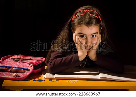 Bored little girl who does not want to study photographed in studio with black background