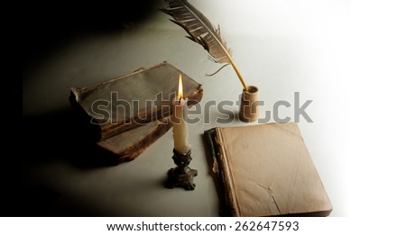 White feather in the inkwell, burning candle and couple of an old burned books