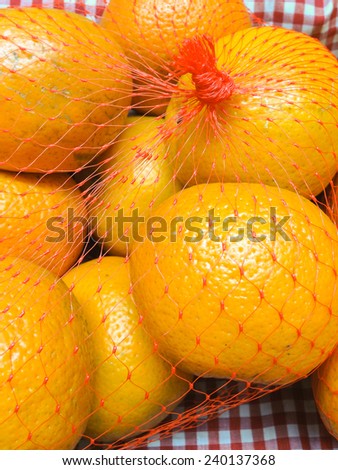 Bunch of oranges in a pink net bag on e red and white check table cloth.