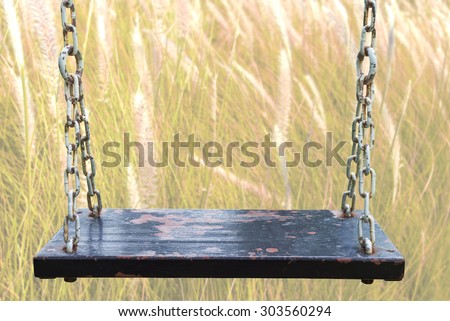 Rusty wood swing and wild flowers blurred background.  Soft focus on wood board.