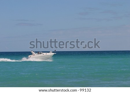 A fast boat cruises across the ocean in front of a beach.