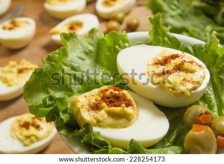 two deviled eggs on a plate with others being prepared on a cutting board in background \