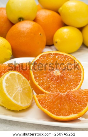 fresh cut orange and lemon on a plate with whole oranges and lemons in background on a white tablecloth.\