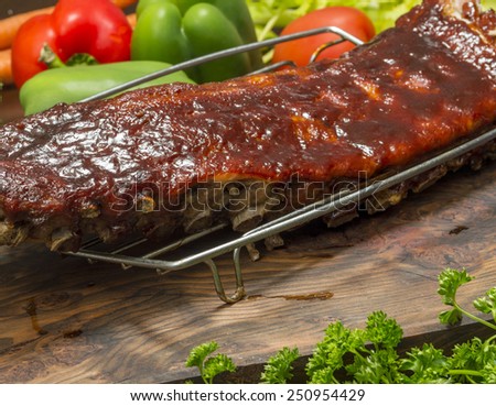 slab of BBQ baby back pork ribs on a cutting board with fresh vegetables behind\