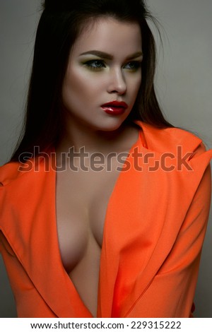 Fashion beauty female model with big breasts red lips and orange jacket