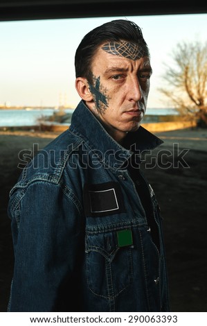 Outdoor Portrait of adult Guy with tattooed Face in denim Jacket on Street