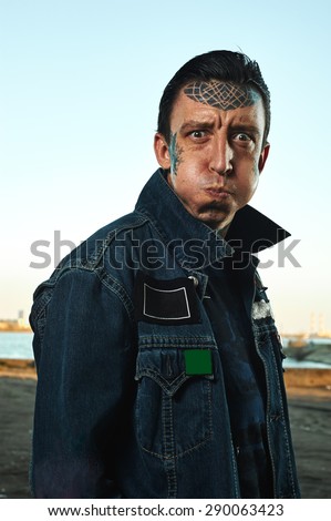 Man with tattooed Face in denim Jacket on Street puff up his Cheeks