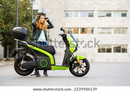 red-haired woman puts on her helmet next to her motorbike parked on the street Foto stock © 