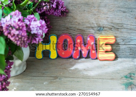 Lilac flowers in a pot and HOME letters on the wooden table