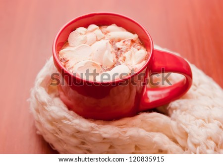A cup of cacao with marshmallow wrapped in a cozy scarf