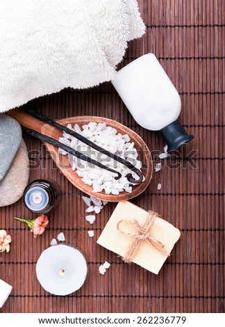 Spa still life with sea salt, soap and vanilla pods on brown mat, top view