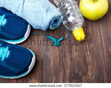 Sport equipment. Sneakers, water, towel and earphones on the wooden background