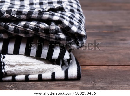 Stack of black and white clothes with striped and checkered patterns on the wooden table close-up