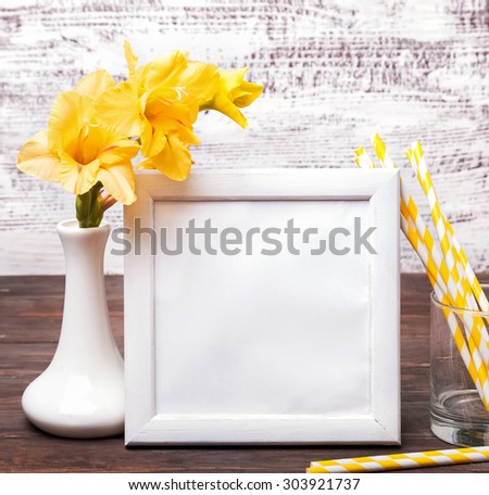 White empty frame with place for text or picture on the table with yellow flowers in a vase and striped paper straws in a glass. Mock up.