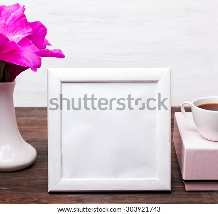 White empty frame with place for text on the table with pink flowers in a vase, pink box and a cup of coffee. Mock up.