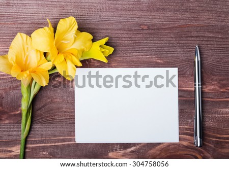 Yellow flower, empty paper sheet and pen on the wooden table, top view