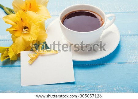 Blank paper card, yellow flowers and coffee on blue colored wooden background close-up