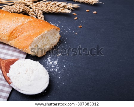 Flour, bread and wheat ears on black background, close-up