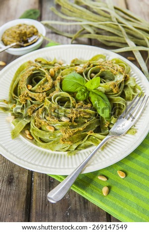 Cooked homemade spinach pasta with pesto, pine nuts and basil leaves served over the rustic wooden table