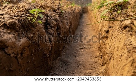 Dig a trench. Earthworks, digging trench. Long earthen trench dug to lay pipe or optical fiber. Construction the sewage and drainage. View from the trench. Clay soil. Part of the image is blurred Сток-фото © 