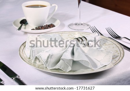 Restaurant place setting with fan napkin in ring and warm coffee in background