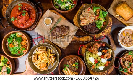 Assorted food set on table, Pasta with seafood, steak ribeye, club sandwich, turkey with black rice, salad with kinoa, tartar from beef, fried loungustine