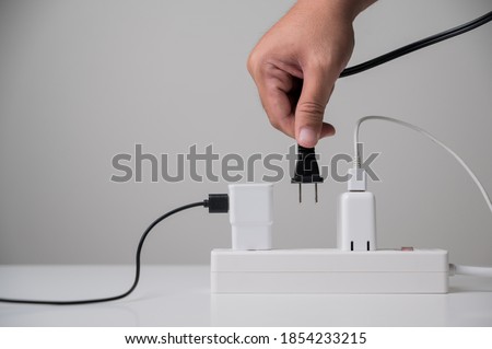 Hand holding Electric plug put on multiple socket. Electrical equipment, electrical wires and power strips in the house. Earth Hour saving electrical energy.