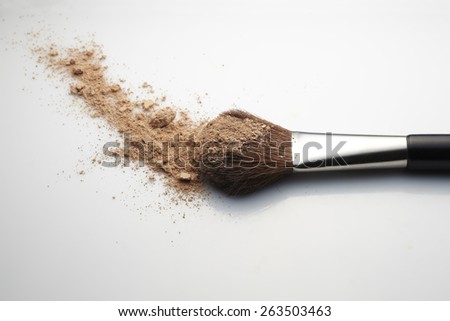 Makeup Brush with beige loose Face Powder placed horizontal on white gradient background.