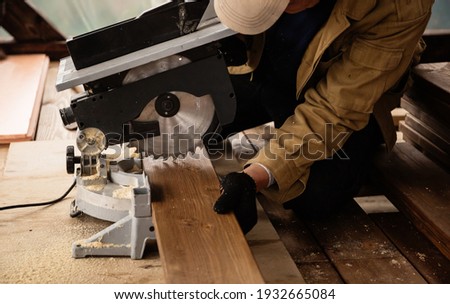 Miter saw with a large metal blade in the hands of a carpenter. Working tool for sawing wooden planks. A close-up of the sawing process. Labor protection and safety rules for the use of power tools. Foto stock © 