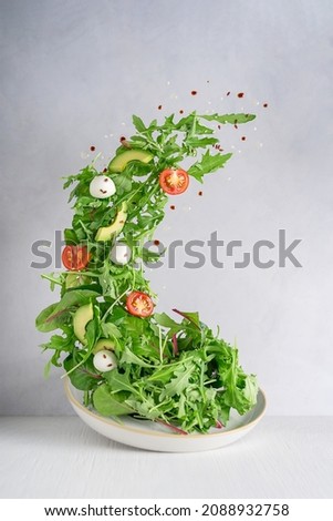 Levitation or flying of vegetarian green salad made of rocket leaf or arugula, sliced cherry tomatoes, avocado slices, Mozzarella italian cheese with drops of balsamic vinegar and olive oil on plate Сток-фото © 