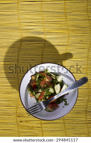 Tomatoes and cucumbers in a plate with a fork on a yellow bamboo mat lit studio lights, the view from the top.