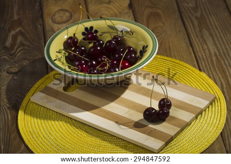 Berries cherry in a plate on a cutting board, mat and yellow wooden background, studio lights lit, the view from the top.