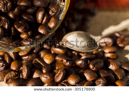 Grains of roasted Arabica coffee with a metal spoon on a background of wooden planks, natural light.