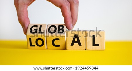Local or global symbol. Businessman turns wooden cubes and changes the word 'local' to 'global'. Beautiful yellow table, white background. Business and local or global concept. Copy space.