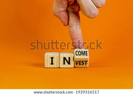Invest or income symbol. Businessman turns a wooden cube and changes the word 'invest' to 'income'. Beautiful orange background, copy space. Business and invest or income concept.
