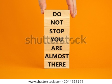 You are almost there symbol. Wooden blocks with words 'do not stop you are almost there'. Businessman hand. Beautiful orange background, copy space. Business, motivation and almost there concept. 商業照片 © 