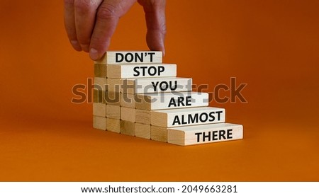 You are almost there symbol. Wooden blocks with words 'dont stop you are almost there'. Businessman hand. Beautiful orange background, copy space. Business and almost there concept. 商業照片 © 